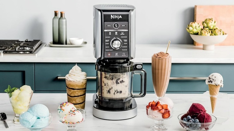 A Ninja ice cream machine on a counter surrounded by numerous ice cream desserts