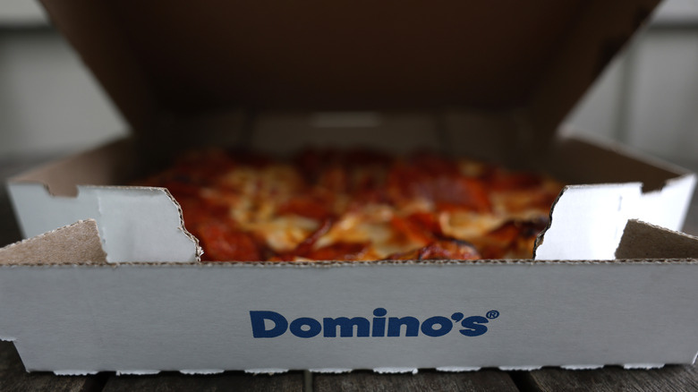 A cardboard Domino's box with an out of focus pizza inside