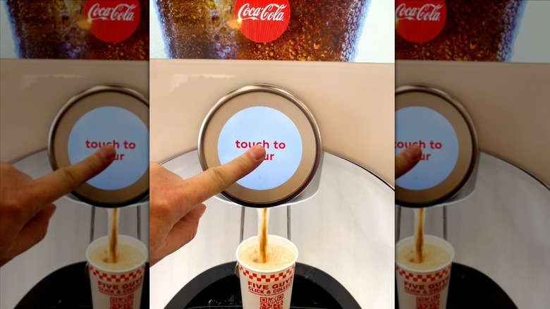 Someone filling up a Five Guys cup at a Coca-Cola Freestyle machine