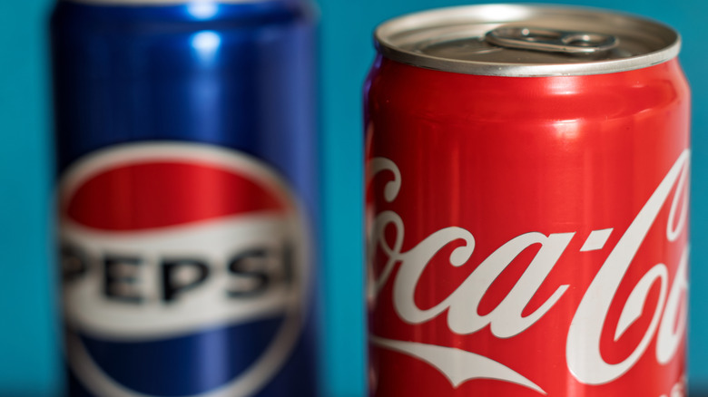 A can of Coca-Cola in focus with a out of focus Pepsi can to the rear left