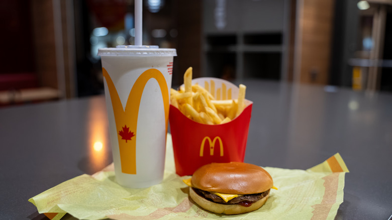 A McDonald's cheeseburger, french fries, and a drink sitting on a table