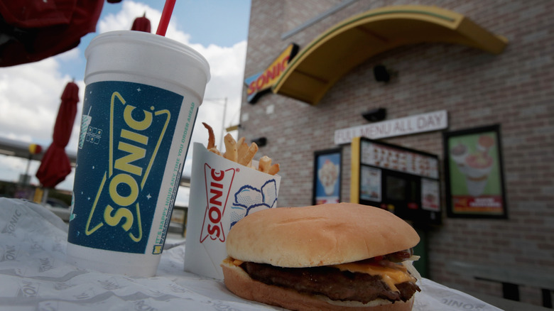 A Sonic combo featuring a hamburger, fries, and a drink on a table outside
