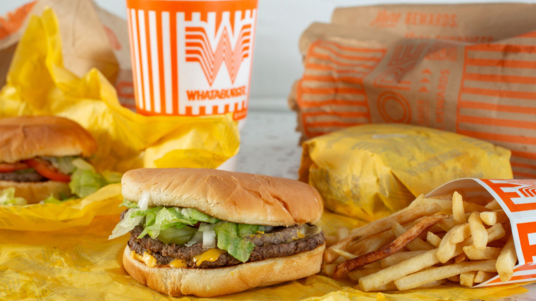 Whataburger hamburgers, fries, and a drink cup in the background