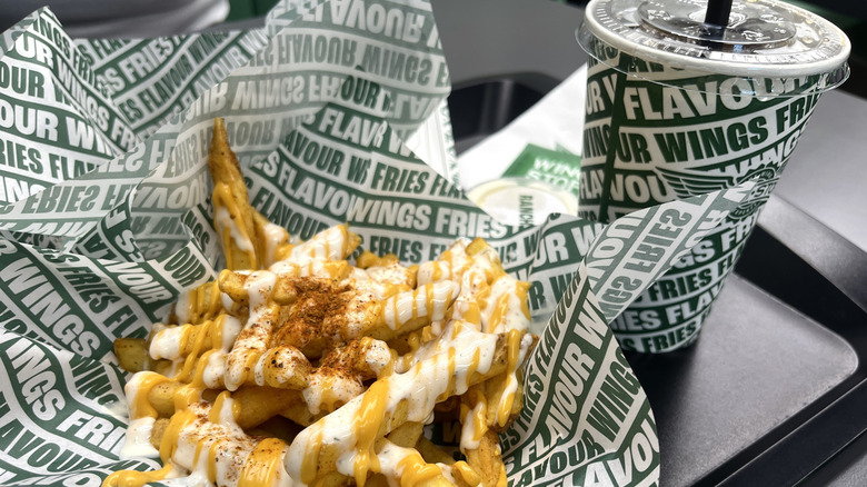 An order of some kind of loaded fries next to a drink cup from WingStop