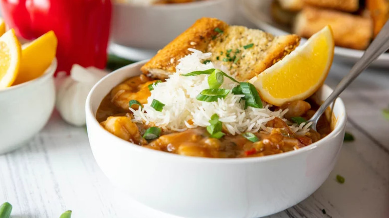 A bowl of etoufee topped with white rice and a lemon wedge