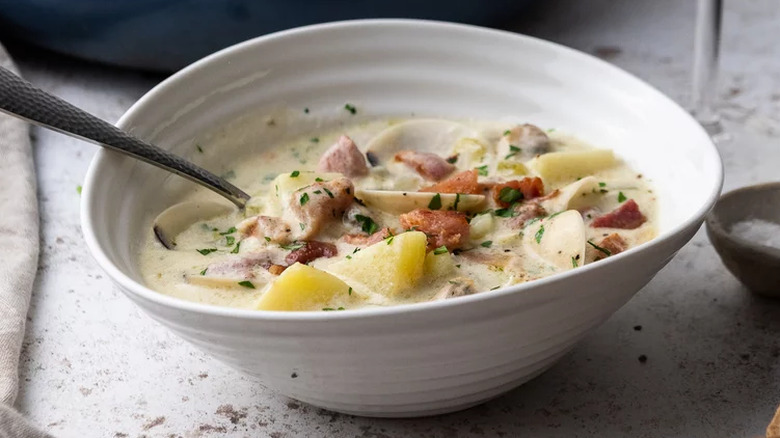 A white bowl of New England clam chowder with a spoon