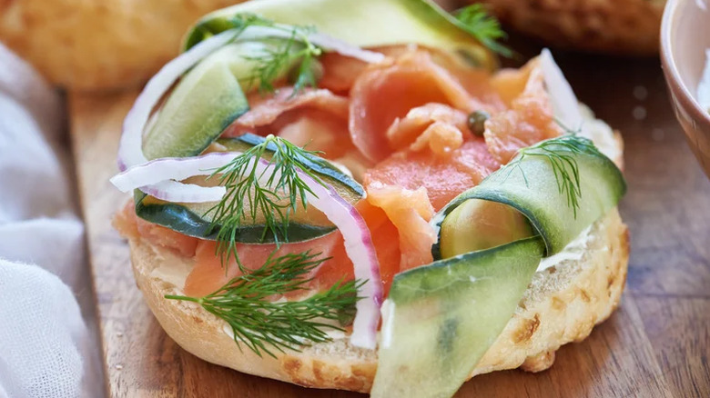 An open bagel of lox, cucumber, dill, and onion