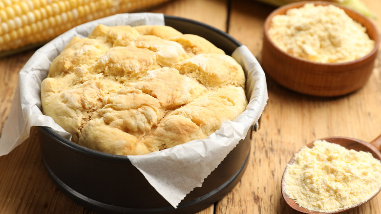 Cornbread alongside fresh corn cobs and cornmeal on wooden table