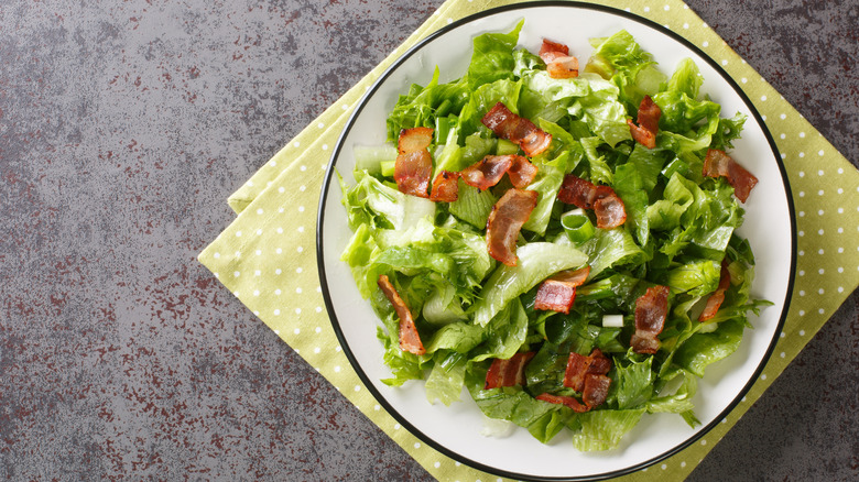 Wilted lettuce salad with bacon and green onions on white plate