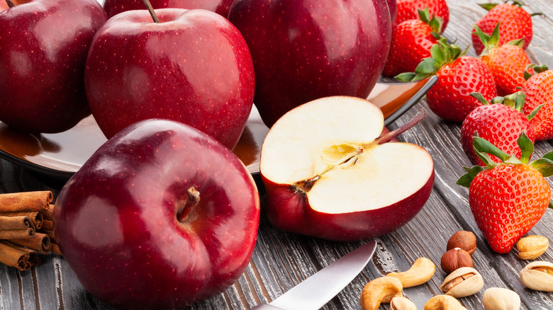 Sliced and whole Red Delicious apples with nuts and strawberries on a grey wooden table
