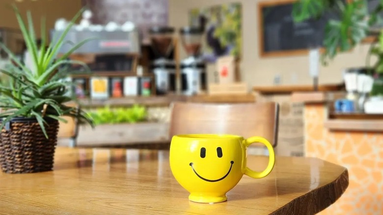 Yellow coffee cup with a smiley and potted plant on table at Higher Grounds Coffee Bar