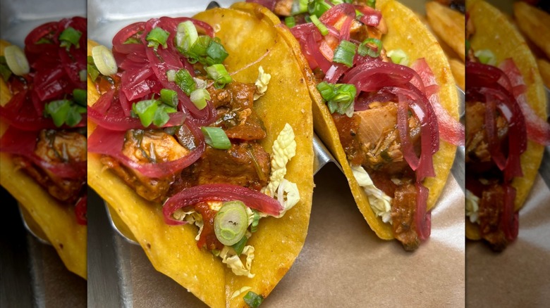 Two tacos on a tray with pickled onions and diced scallions