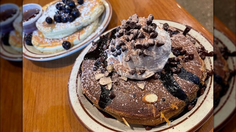 Two plates with stacks of chocolate and blueberry pancakes