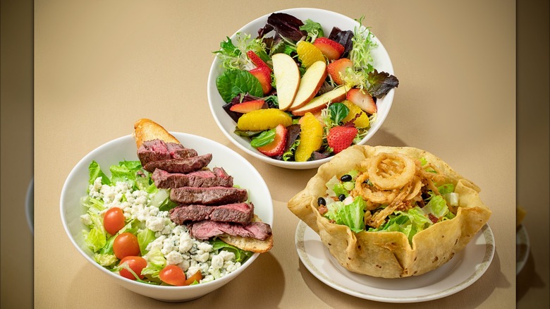 Salads with steak, fruits, and onion rings on brown background