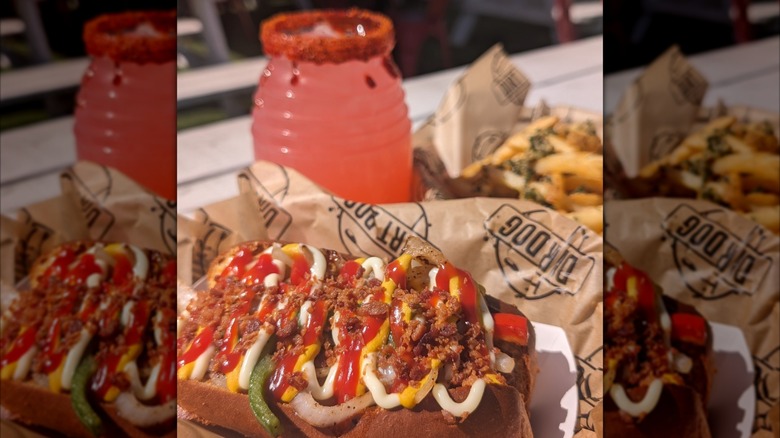 Loaded hot dog with fries and a drink in the background
