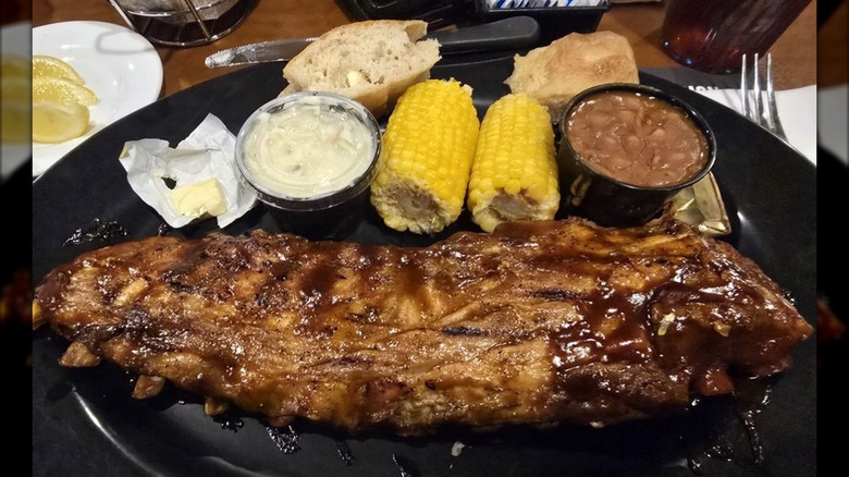 Rack of ribs on black plate with corn, beans, butter, and bread