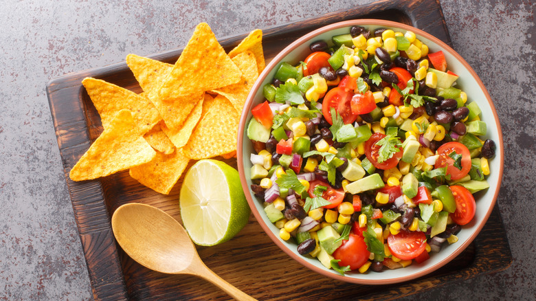 Cowboy caviar on a wooden tray with a lime and tortilla chips on the side.