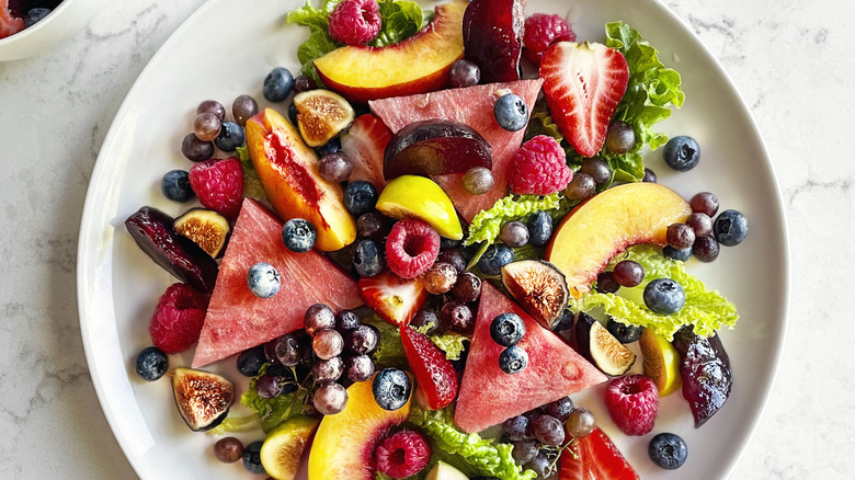 Fruit salad on a plate featuring watermelon, peaches, berries, figs, grapes, and lettuce.