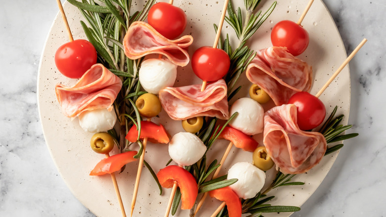 Prosciutto skewers with tomato, mozzarella, and olives on a plate with sprigs of rosemary.