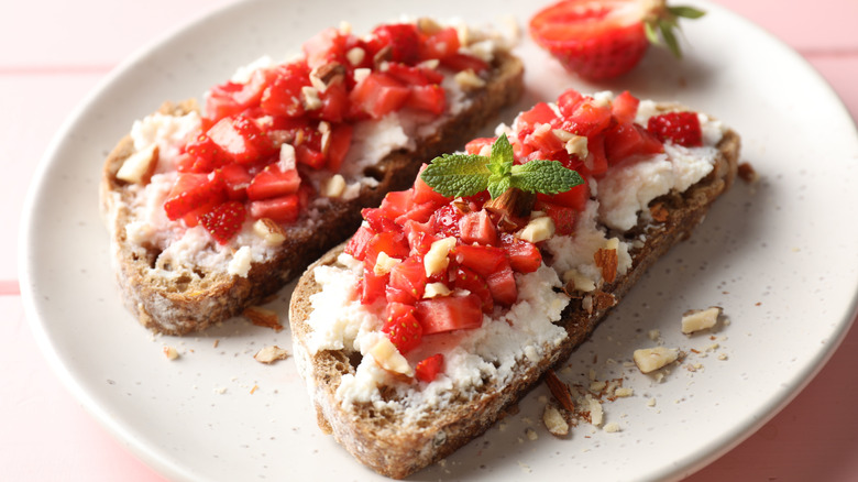 Strawberry bruschetta with cheese and mint leaves on a white plate.