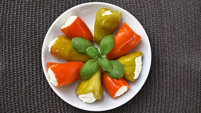 Plate with seven mini pepper stuffed with cream cheese on it.