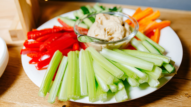 Round plate with sticks of celery, red pepper, cucumber, and carrot surrounding a ramican of spread.