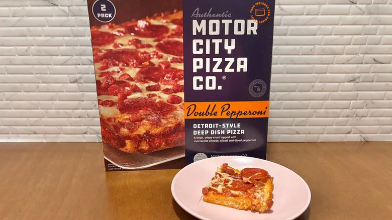 Box of the Motor City Pizza Co Detroit-style deep dish pizza with one baked slice on a plate