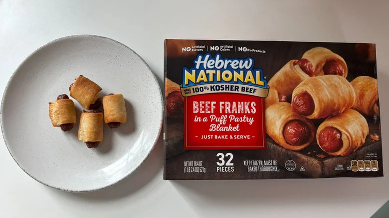 Four pieces of Hebrew National beef franks in puff pastry on a plate and a box of franks next to it