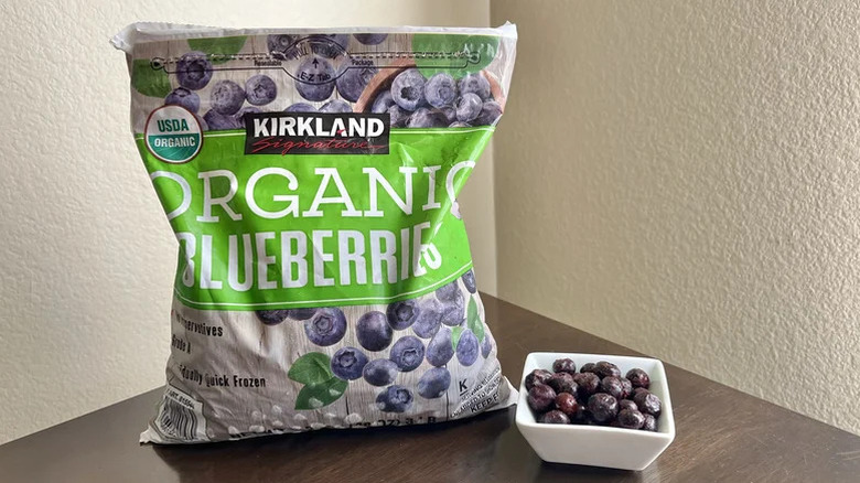 Bag of organic blueberries on a table with a handful of frozen berries in a white dish