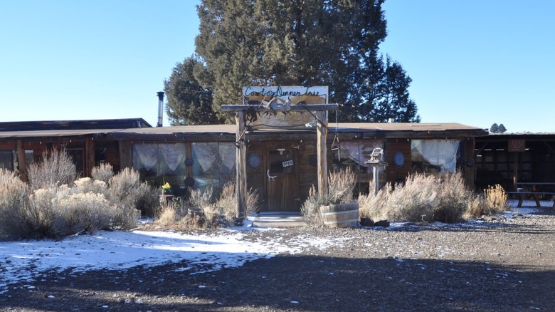 Single-story wooden building in front of a large tree with snow on the ground