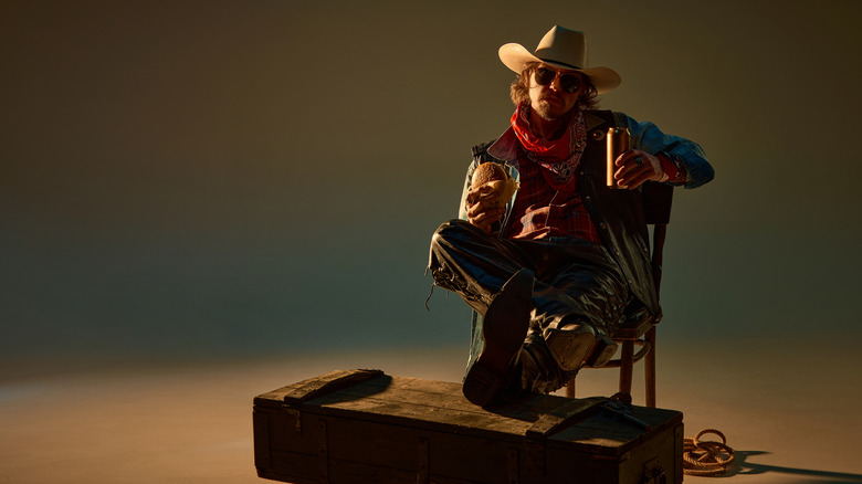 A man dressed as a cowboy holding a burger and a beer