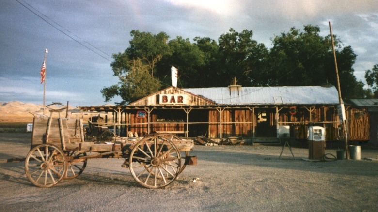 A wooden building with bar sign and gas pump, with frame of a wagon in the desert