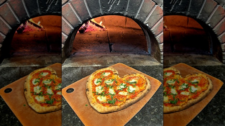 Heart-shaped pizza sliding into wood-fired oven