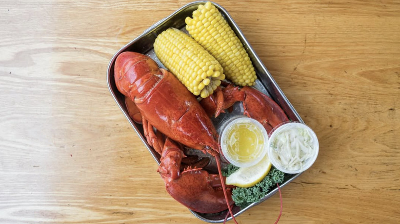 a steamed lobster with corn and sides on a silver tray on a wood background