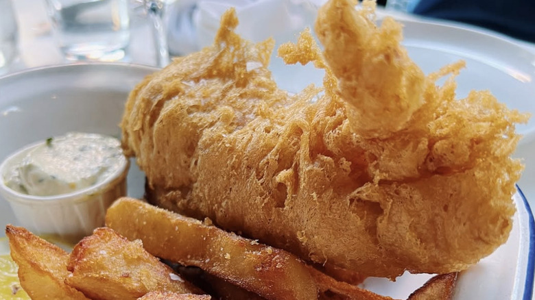 close up of fish and chips with fries and a dipping sauce.