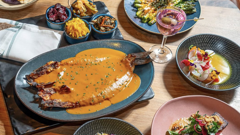 a sauce covered fish filet surrounded by other small plates and cocktails