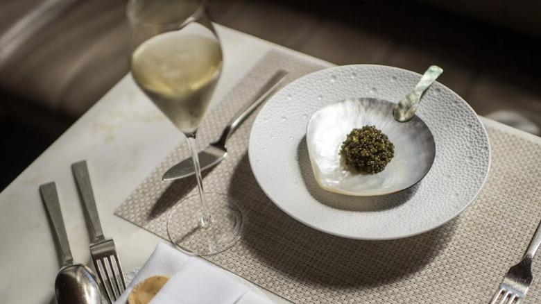 a glass of wine alongside caviar on a shell