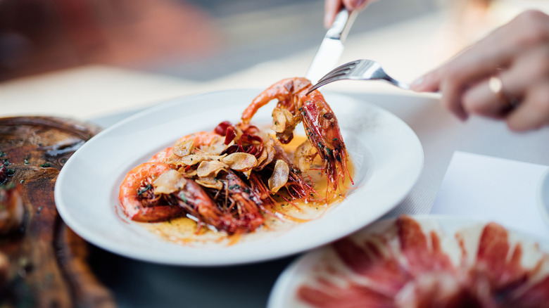 a plate of langoustines in sauce with a hands holding cutlery