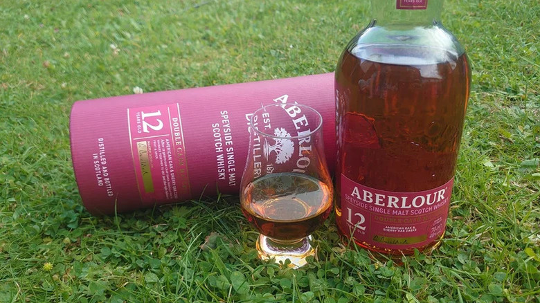 A bottle of Aberlour 12-year single malt whisky posed on grass next to a filled glass and its box
