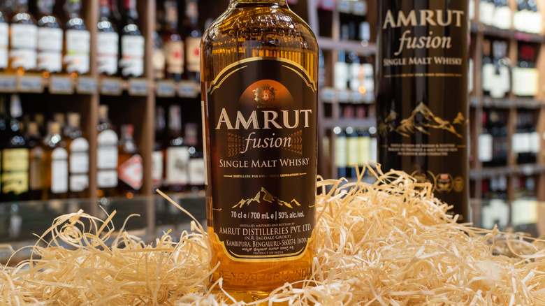 A bottle of Amrut Fusion single malt whisky posed among straw within a liquor store