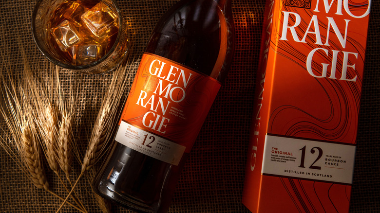 A top-down view of a bottle of Glenmorangie 12-year next to ears of barley, a filled glass with ice, and its box