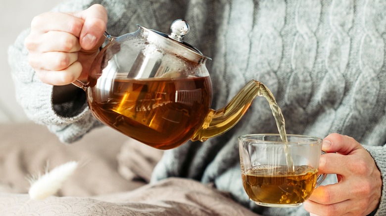 Person pouring tea from glass teapot