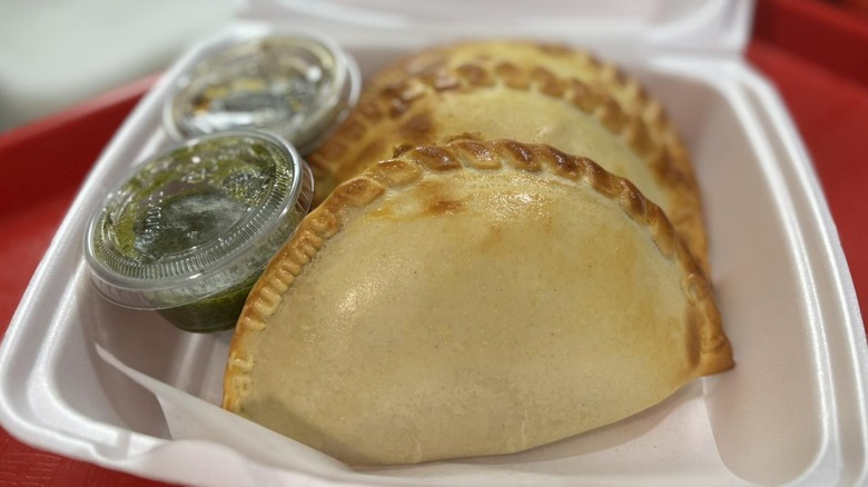 Two empanadas and salsa verde in a Styrofoam box