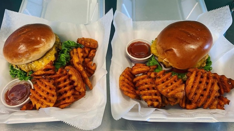 Two burgers, ketchup, and crinkle fries in Styrofoam boxes
