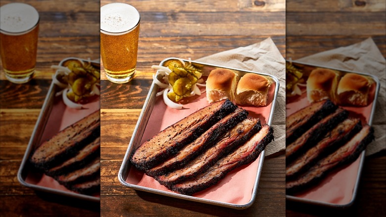 Brisket with bread rolls and pickles on tray and glass of beer