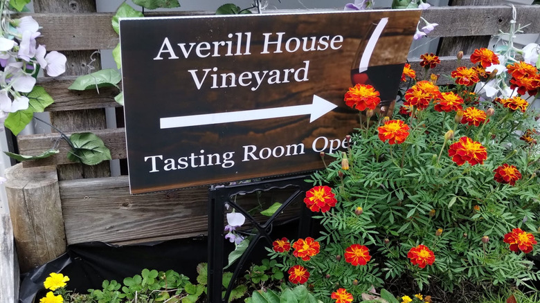 A wooden sign directing patrons to the Averill House Vineyard tasting room, surrounded by flowers