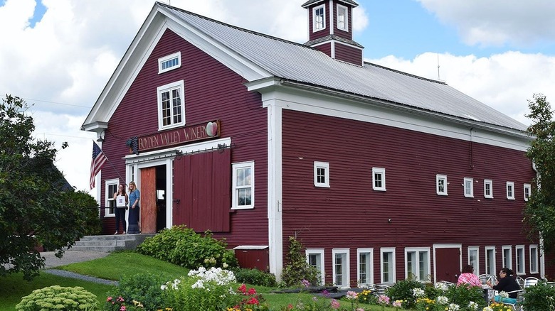 A red farmhouse winery exterior with two women on the front steps, surrounded by flower beds
