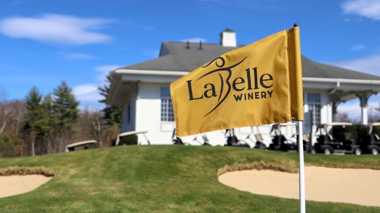 A portion of the golf course at LaBelle Winery, with golf carts and a white building behind a yellow LaBelle flag