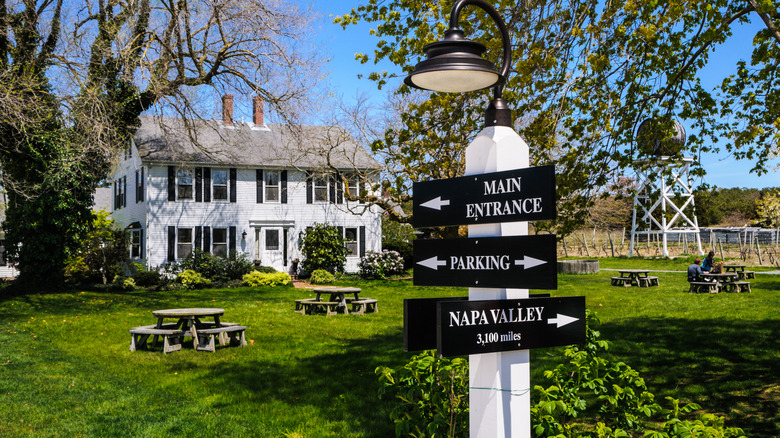 Truro winery exterior with picnic tables scattered around the lawn, with the vineyards to the right and a directional sign at the forefront