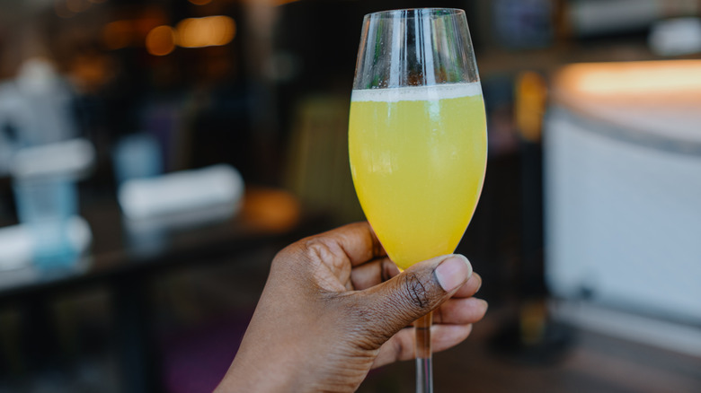 A hand holding a glass of mimosa